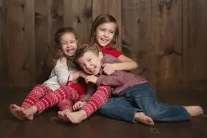 Three siblings laughing together during a family photography session in Cincinnati, wearing festive red and cozy outfits