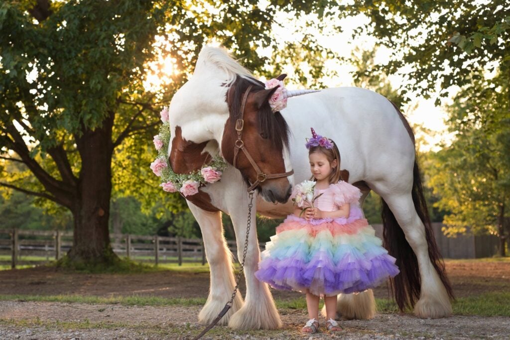 Young girl in rainbow tutu dress with a unicorn-themed horse decorated in flowers.