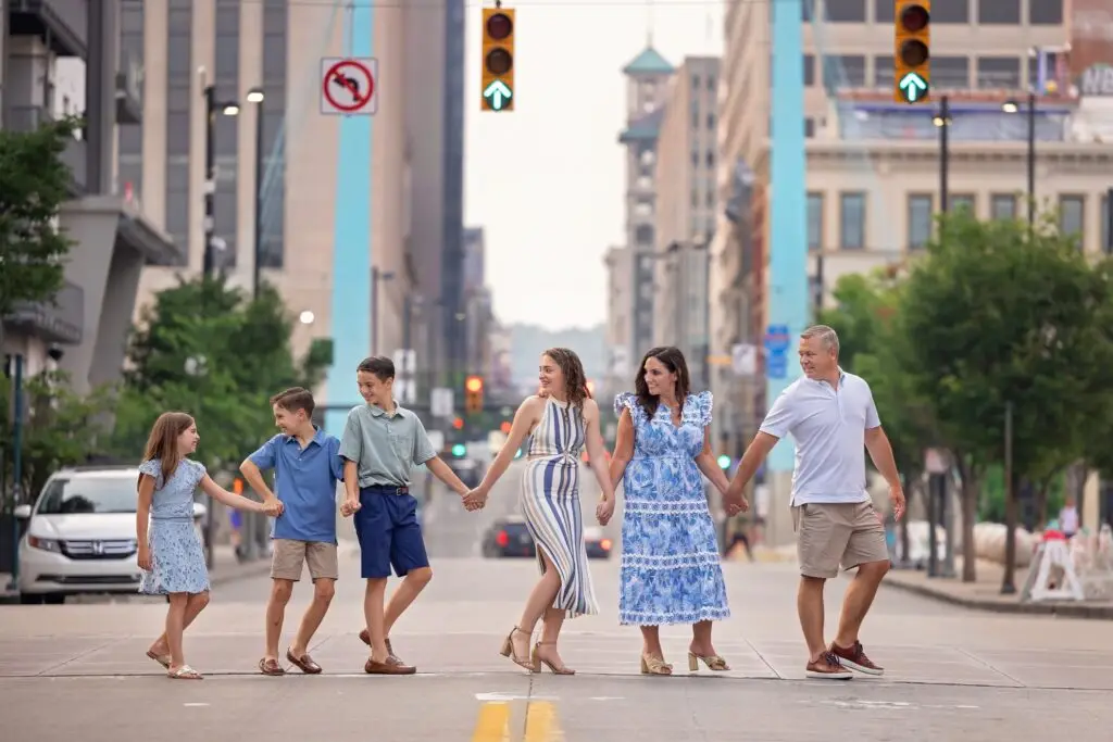 Cincinnati family photo outfit inspiration in downtown crosswalk – Cream N Cocoa A family of six walks hand-in-hand across a downtown Cincinnati street wearing coordinated blue and neutral outfits—perfect inspiration for summer family photos.