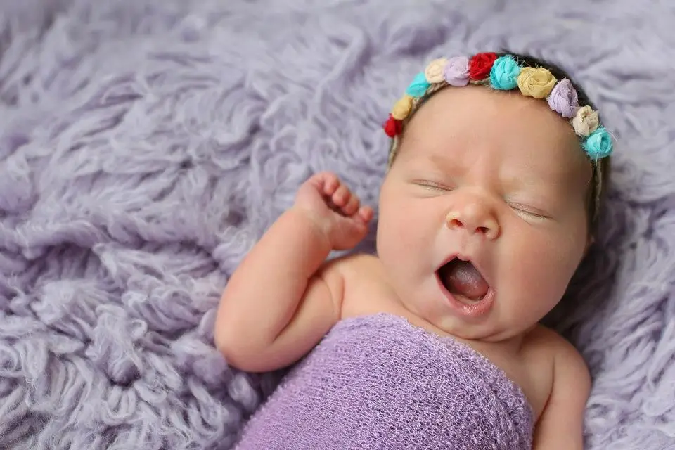 awning newborn girl swaddled in a purple wrap on textured lavender blanket with rainbow flower headband