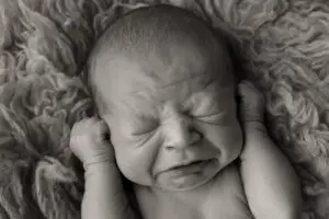 Black and white close-up of a newborn mid-sneeze with hands near ears, captured during a candid moment in a Cincinnati newborn photography session.