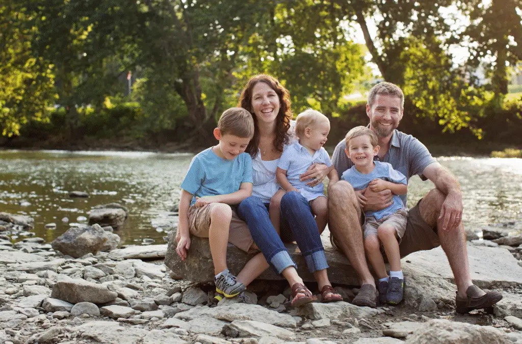 Smiling family sitting on river rocks during an outdoor photography session in Cincinnati, Ohio, captured by Cream n Cocoa Photography.