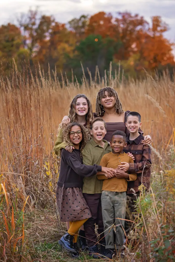 Cincinnati family photographer capturing children sitting in tall grass with fall foliage